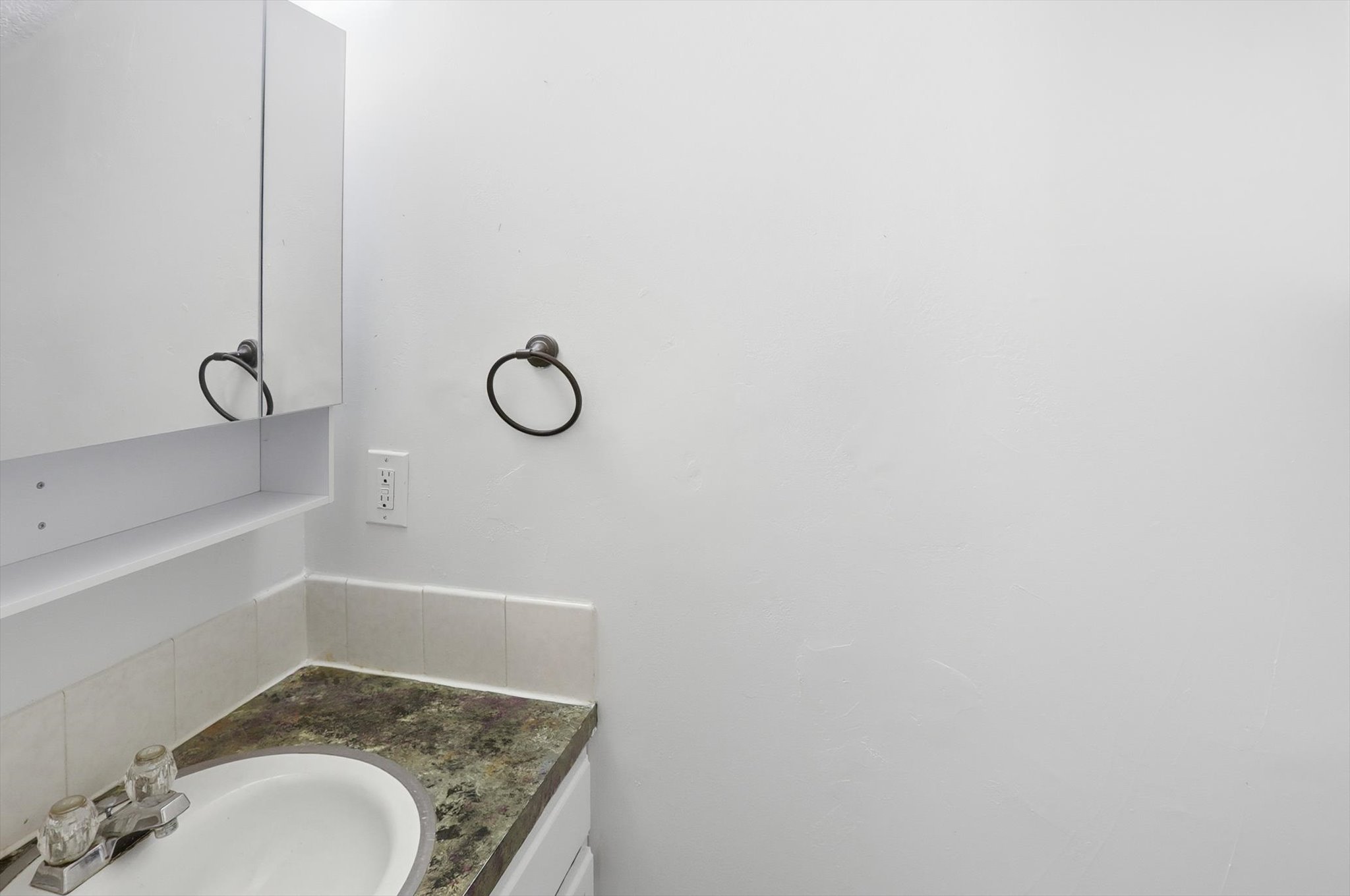 Bathroom vanity featuring an oval undermount sink, a mottled countertop, and a mirrored medicine cabinet with an integrated shelf