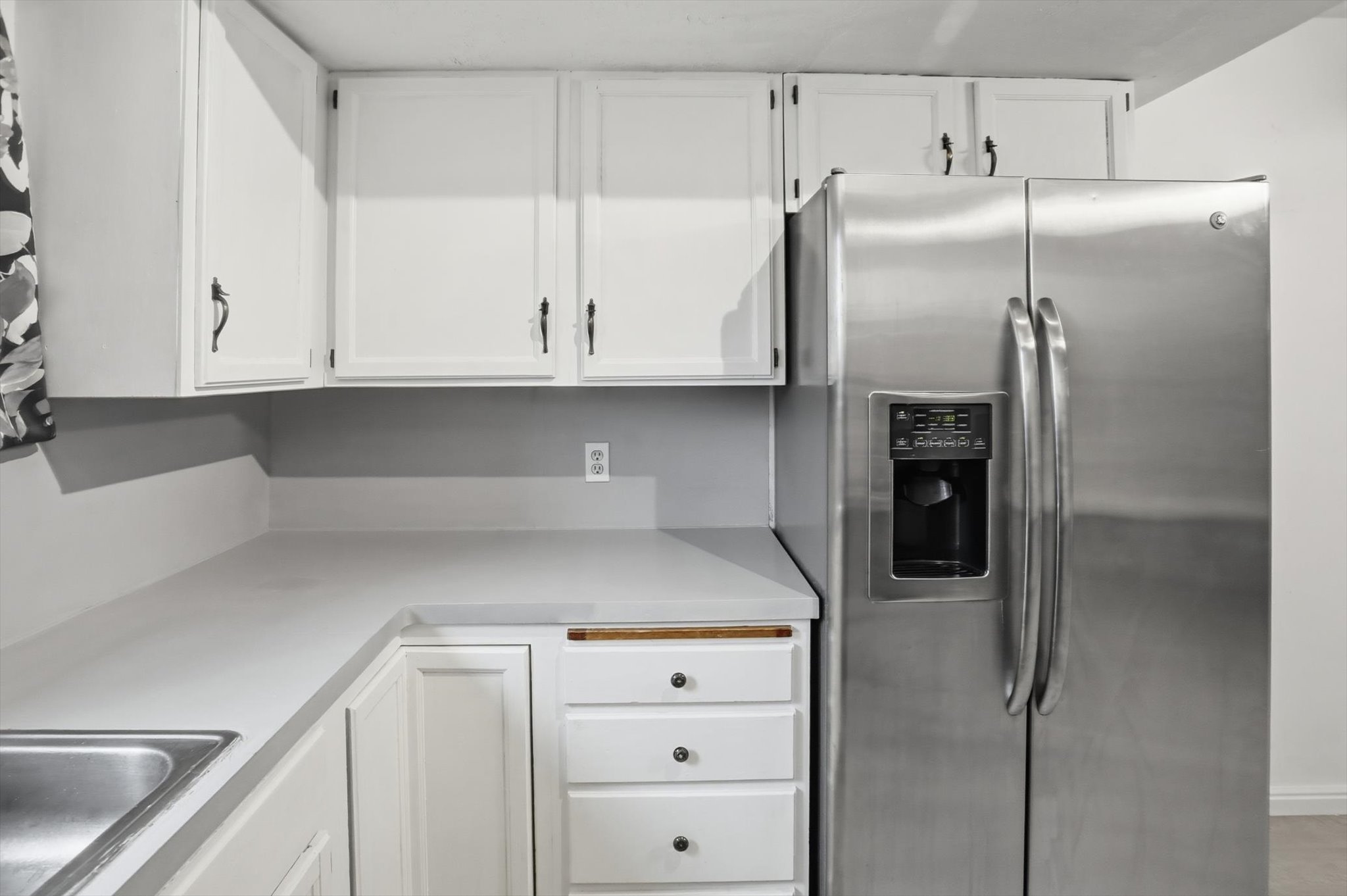 White cabinetry with black hardware, light-toned countertops, stainless steel side-by-side refrigerator with exterior dispenser, integrated stainless steel sink, and drawer storage
