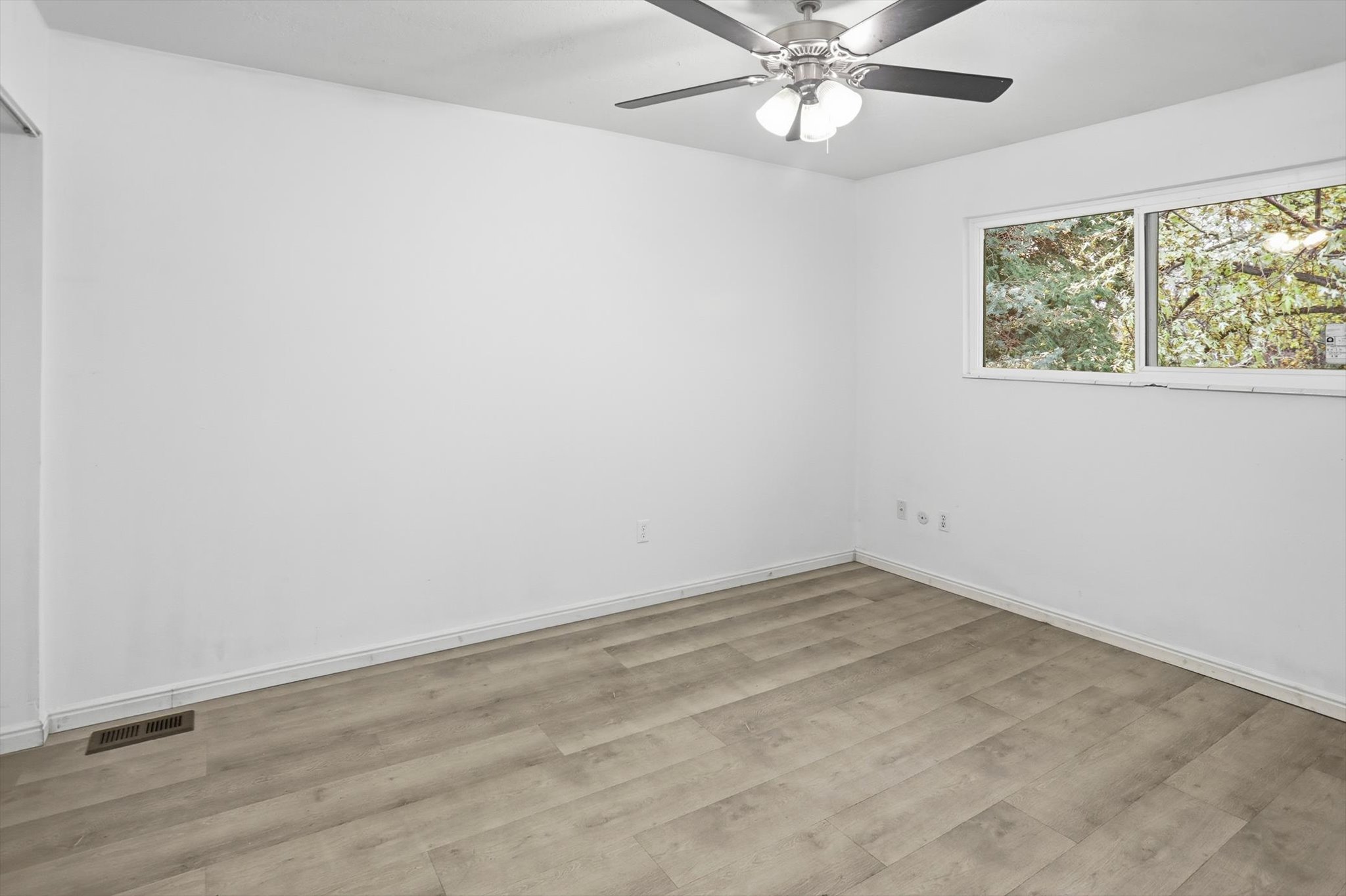 Bright interior space featuring wood-finish flooring, white walls, and a ceiling fan with integrated lighting