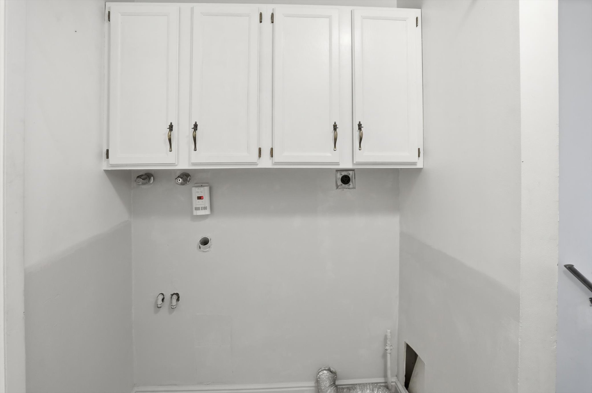 Dedicated laundry area featuring white upper cabinetry with dark hardware and essential plumbing hookups