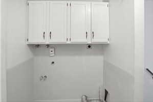 Dedicated laundry area featuring white upper cabinetry with dark hardware and essential plumbing hookups