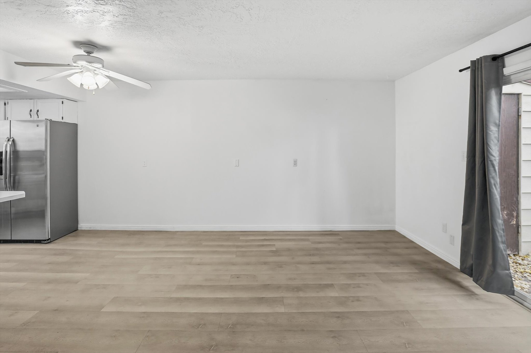 Open-concept living space featuring wood-finish flooring, white walls, and a ceiling fan