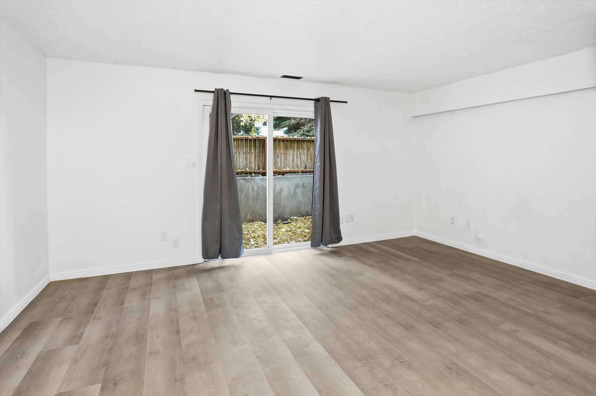 Spacious room featuring new wood-finish flooring, white walls, and bright white trim