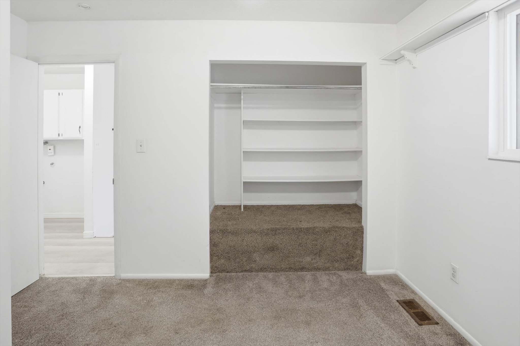 Interior room featuring wall-to-wall carpeting, white painted walls, a built-in closet with shelving and hanging rod, and a single window