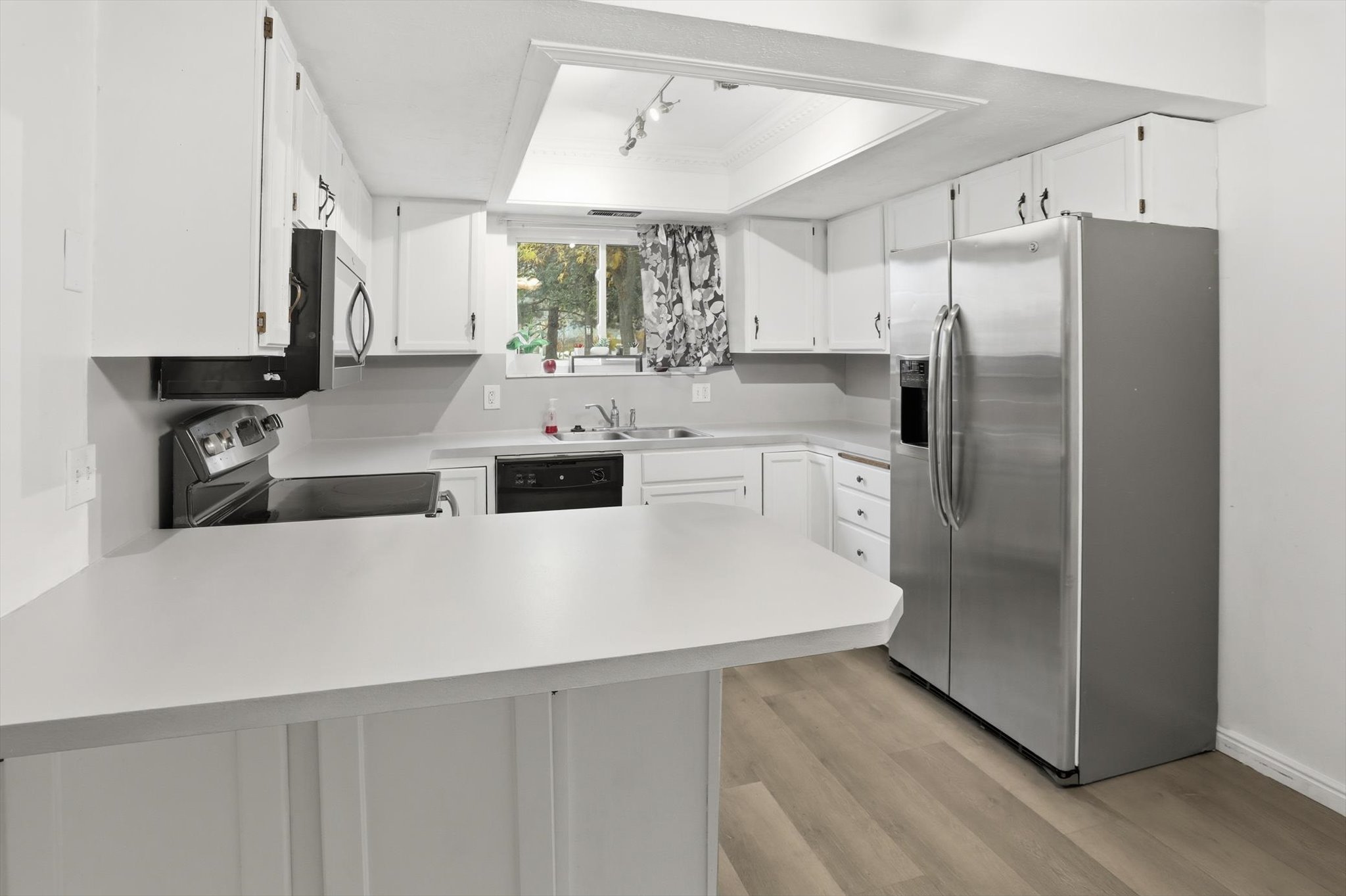 Kitchen featuring white cabinetry, light countertops, wood-finish flooring, stainless steel side-by-side refrigerator, and a built-in cooktop with oven