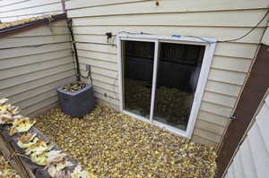 Basement-level exterior featuring light-colored horizontal siding and a white-framed sliding glass door