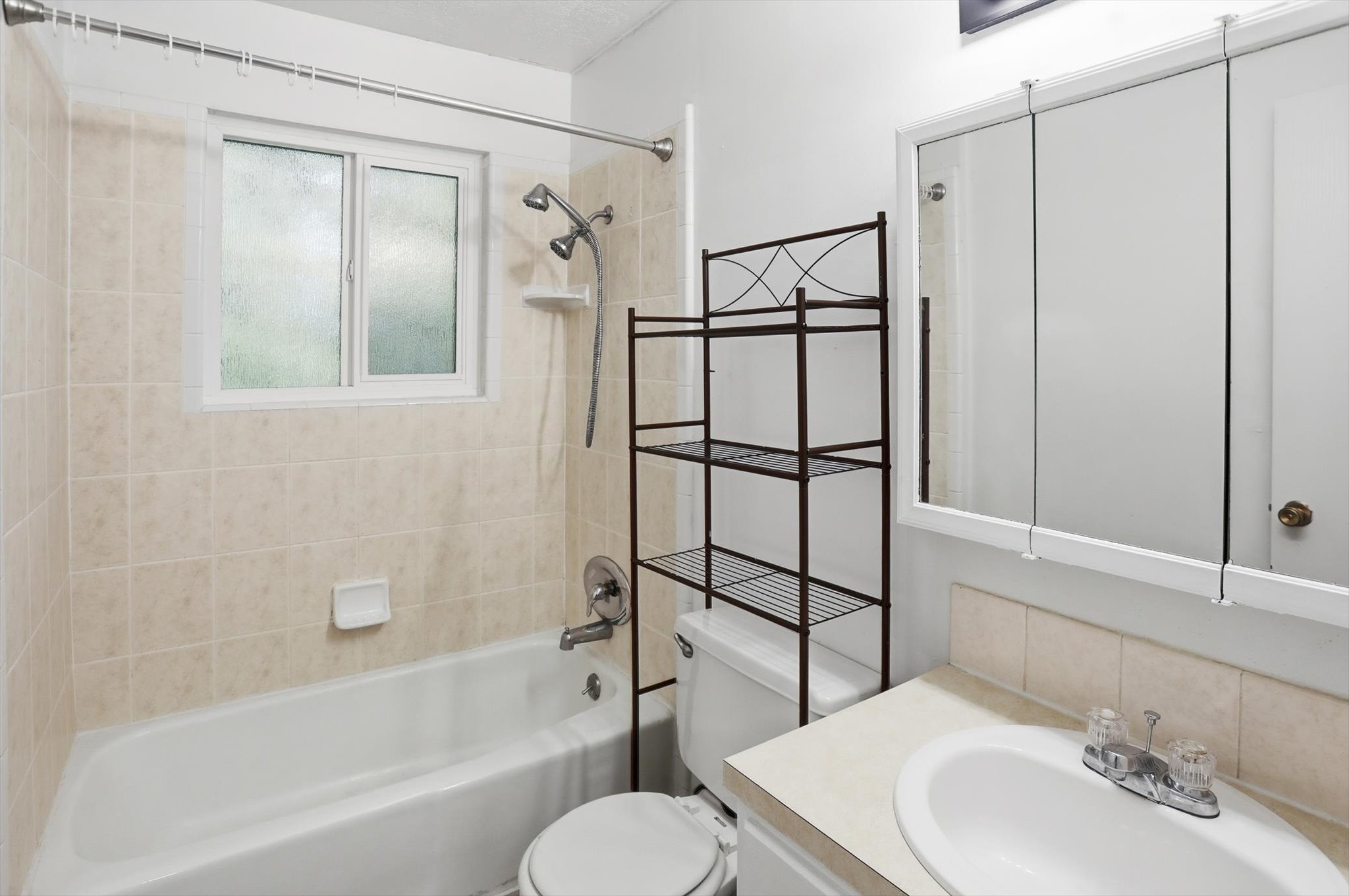 Bathroom featuring a white bathtub, ceramic tile surround with a window, white vanity with an integrated sink, and a mirrored medicine cabinet