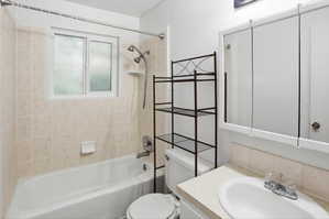 Bathroom featuring a white bathtub, ceramic tile surround with a window, white vanity with an integrated sink, and a mirrored medicine cabinet