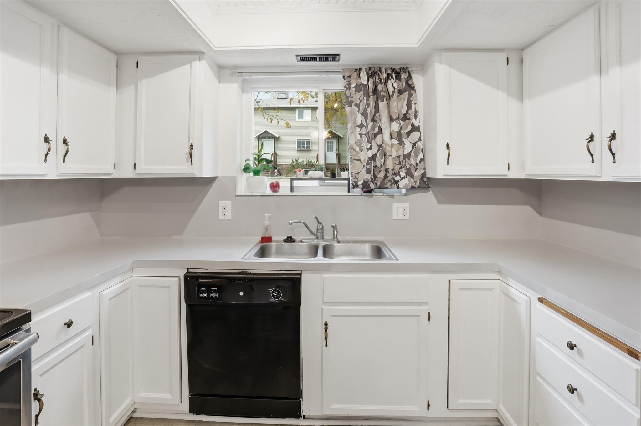 Kitchen featuring white cabinetry, light countertops, and a double basin stainless steel sink with a window overhead
