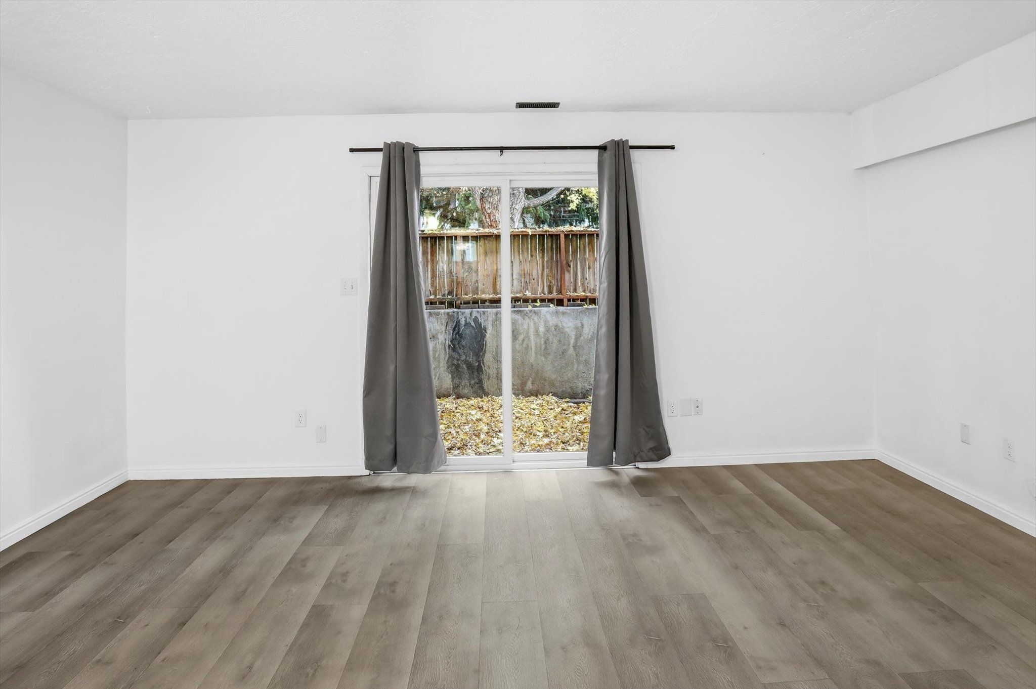 Spacious room featuring wood-finish flooring, white walls, and white baseboards