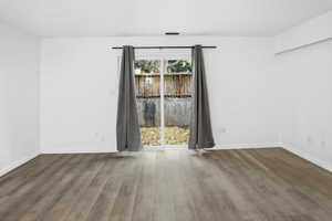Spacious room featuring wood-finish flooring, white walls, and white baseboards