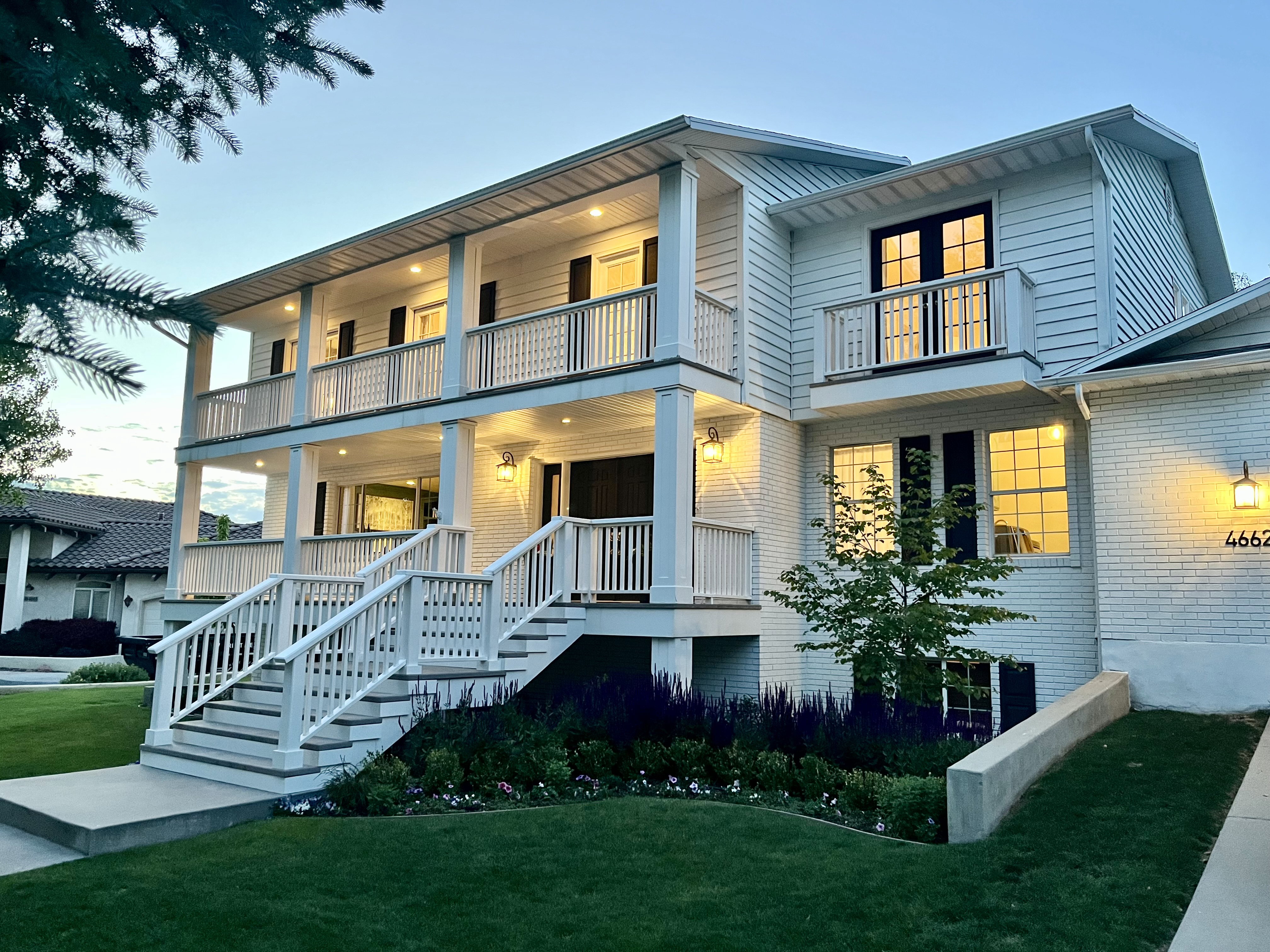 White brick and siding exterior with a multi-level porch, featuring recessed lighting, a prominent staircase, and dark-framed windows