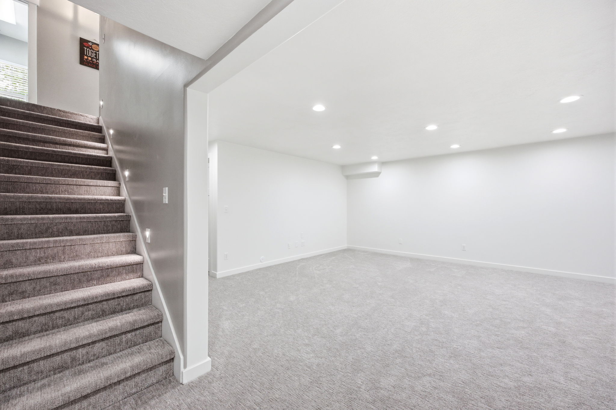 Spacious lower-level room featuring recessed lighting, light-colored carpeting, a neutral wall palette, and a staircase with integrated step lighting