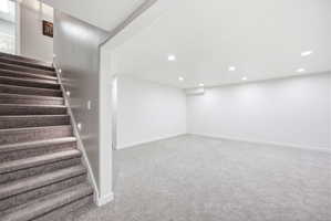Spacious lower-level room featuring recessed lighting, light-colored carpeting, a neutral wall palette, and a staircase with integrated step lighting