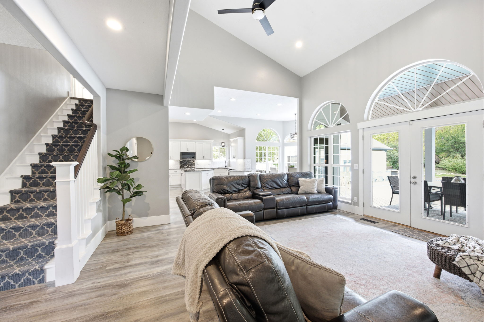 Spacious living area featuring vaulted ceilings, recessed lighting, wood-finish flooring, and a patterned carpeted staircase with white risers and dark wood handrail