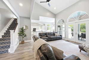 Spacious living area featuring vaulted ceilings, recessed lighting, wood-finish flooring, and a patterned carpeted staircase with white risers and dark wood handrail