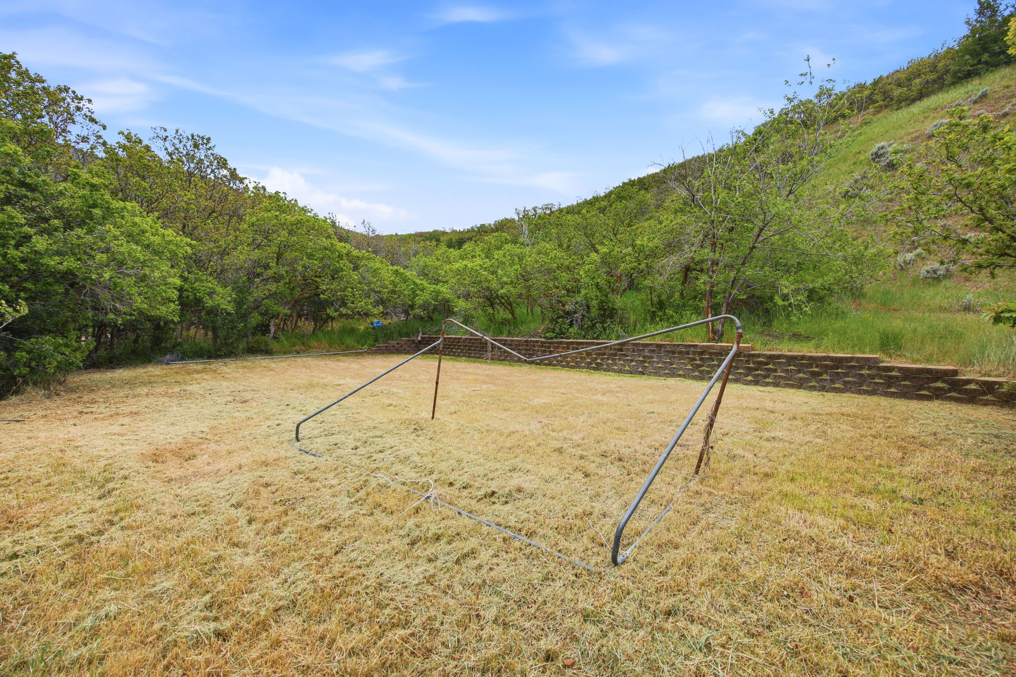 Expansive grassy yard with terraced retaining walls, surrounded by abundant mature trees and natural landscaping