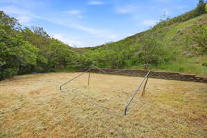 Expansive grassy yard with terraced retaining walls, surrounded by abundant mature trees and natural landscaping