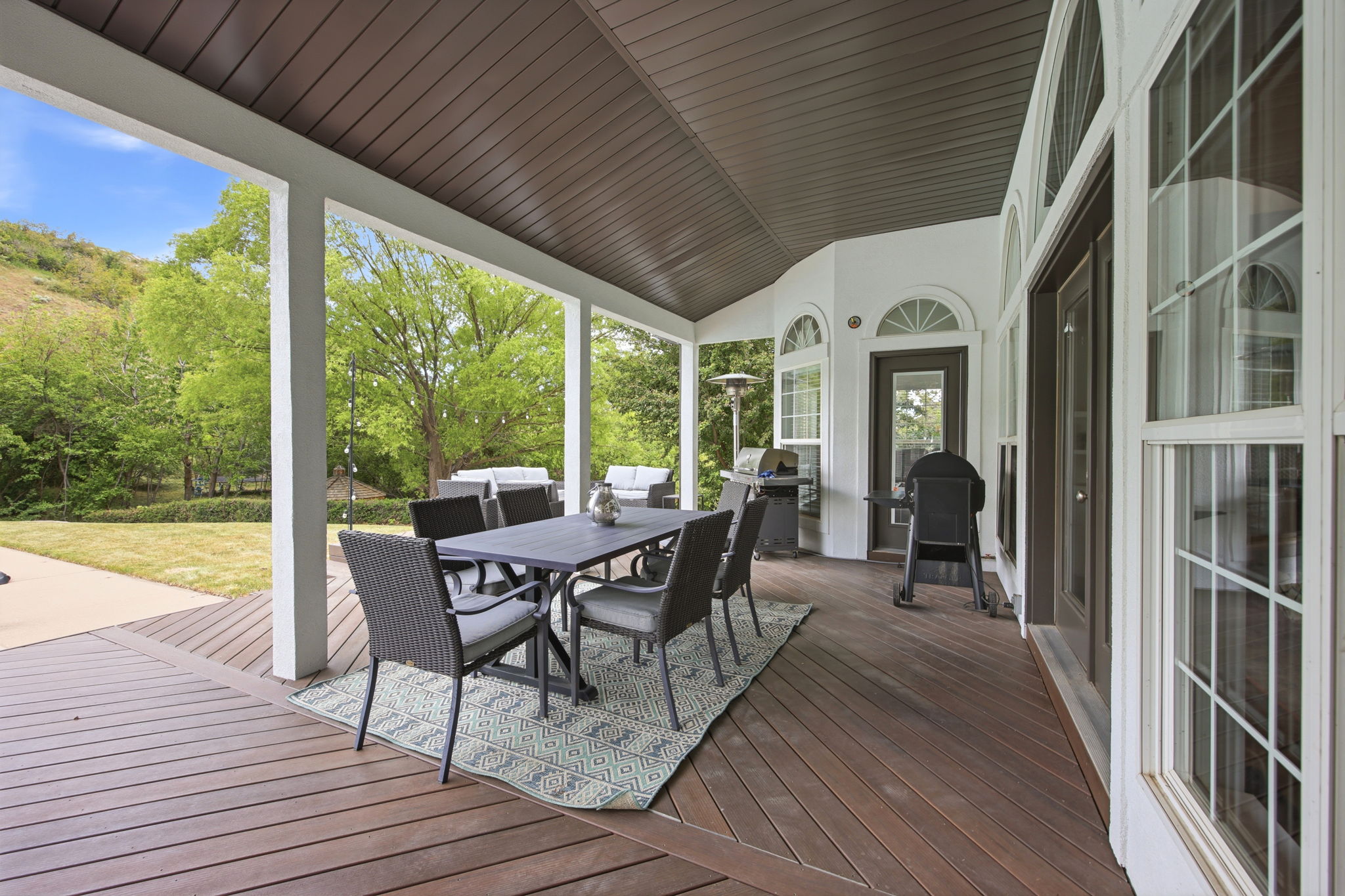 Expansive covered deck featuring wood-finish flooring, white support columns, and a dark brown slatted ceiling