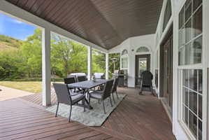 Expansive covered deck featuring wood-finish flooring, white support columns, and a dark brown slatted ceiling