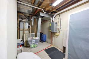 Utility area featuring exposed ceiling joists, overhead fluorescent lighting, concrete flooring, a tankless water heater, and visible ductwork