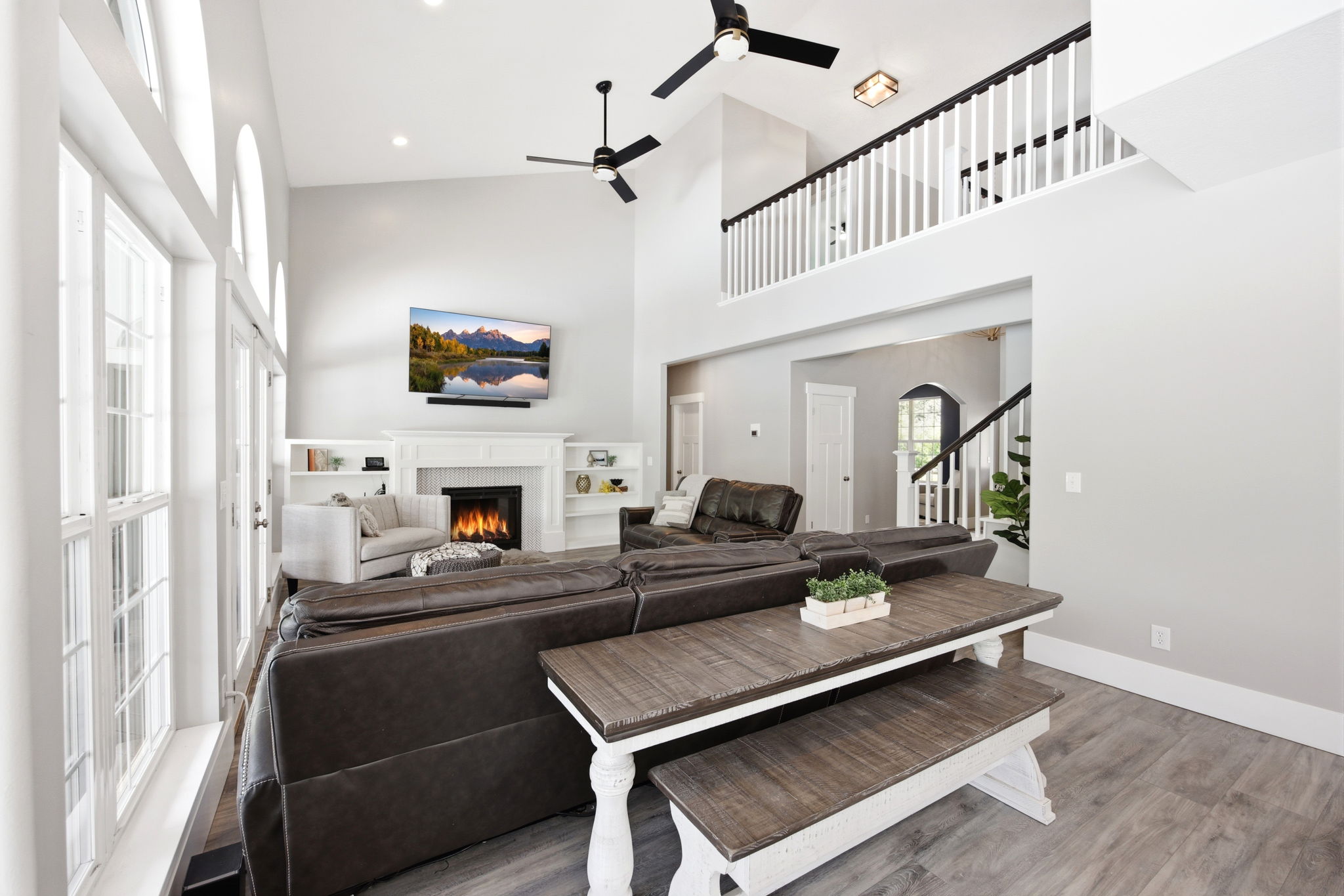 Vaulted ceiling living area featuring a fireplace with white mantle, built-in shelving, wood-finish flooring, and upper-level railing