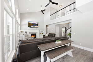 Vaulted ceiling living area featuring a fireplace with white mantle, built-in shelving, wood-finish flooring, and upper-level railing