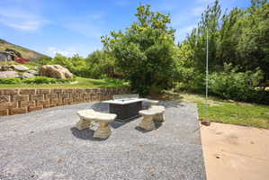 Outdoor entertainment area featuring a rectangular fire pit with glass surround, two stone benches, and a gravel patio surface