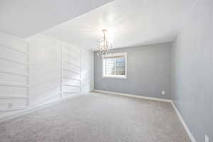 Spacious room featuring a decorative accent wall with geometric paneling, light gray carpeting, and a window with horizontal blinds