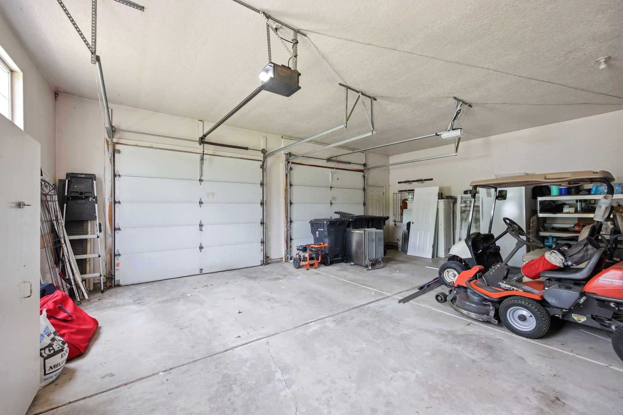 Spacious two-car garage featuring concrete flooring, overhead lighting, and an automatic garage door opener