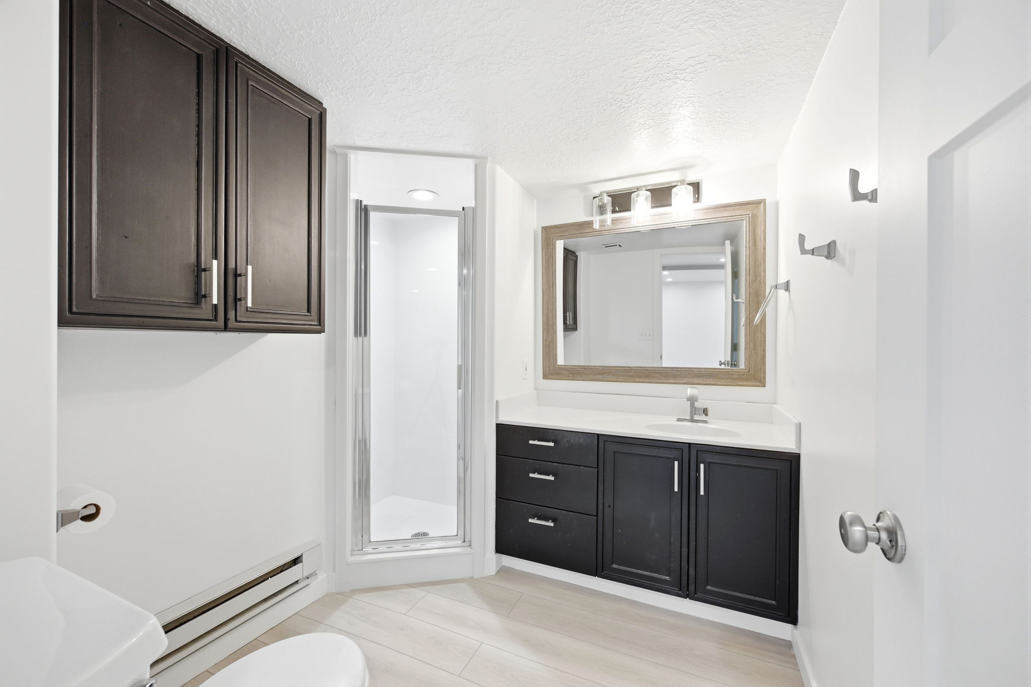 Bathroom featuring dark wood cabinetry, a white countertop, a framed mirror, a vanity light fixture, and a glass-enclosed shower