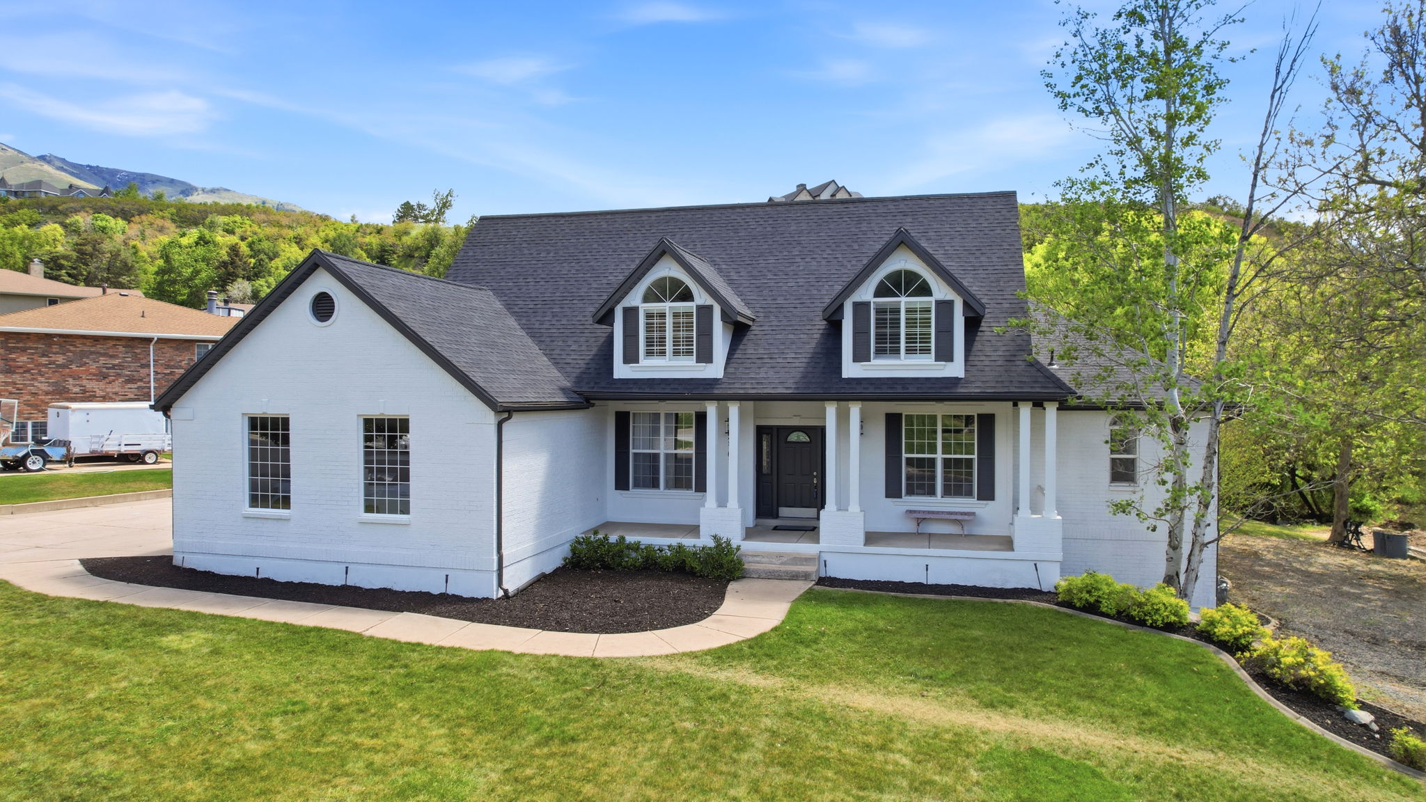 White brick residence with a dark shingle roof and a covered porch