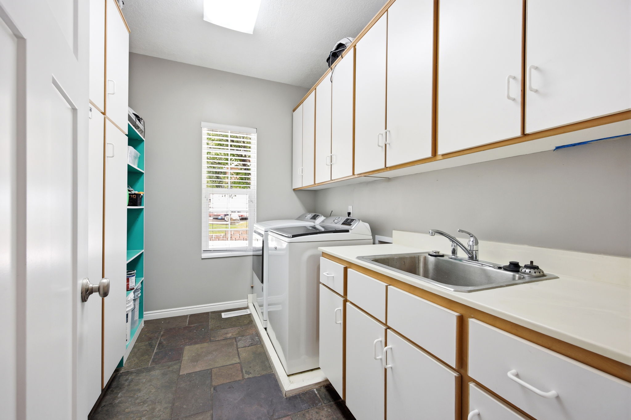 Utility room featuring extensive white cabinetry, a built-in stainless steel sink, large format floor tiling, a window with blinds, and recessed lighting