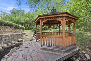 Wooden gazebo with a shingled roof, featuring intricate balusters and a cupola