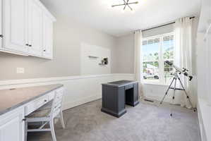 Integrated desk with upper cabinetry, large window, textured accent wall, and built-in shelving