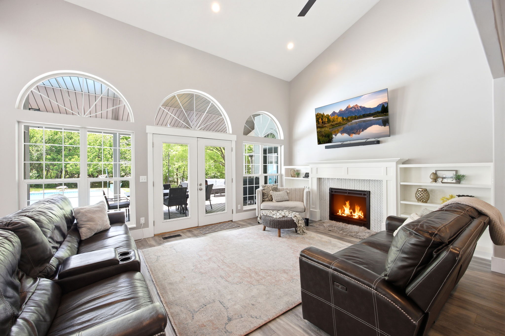 Living room featuring vaulted ceilings, fireplace with built-in shelving, wood-finish flooring, and multiple arched windows with exterior access