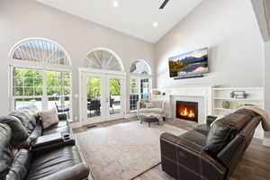 Living room featuring vaulted ceilings, fireplace with built-in shelving, wood-finish flooring, and multiple arched windows with exterior access