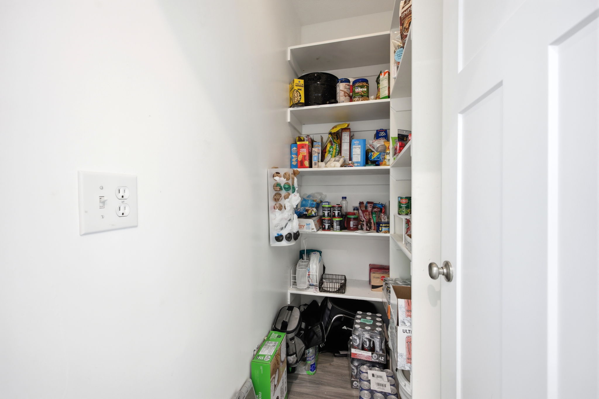 Walk-in pantry featuring extensive built-in shelving, wood-finish flooring, and a white interior door with brushed nickel hardware