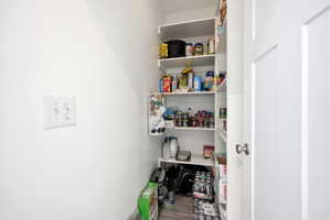 Walk-in pantry featuring extensive built-in shelving, wood-finish flooring, and a white interior door with brushed nickel hardware