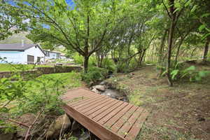 Natural stream and wooded area featuring a wood-finish footbridge, stone retaining walls, and distant mountain backdrop