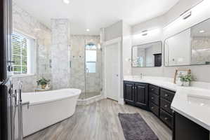 Spacious bathroom featuring a freestanding tub, glass-enclosed shower, dual vanities with dark cabinetry, and light wood-finish flooring