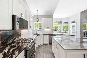 Gourmet kitchen featuring a stainless steel range, white shaker cabinetry, black and grey patterned countertops, a white herringbone tile backsplash, and wood-finish flooring
