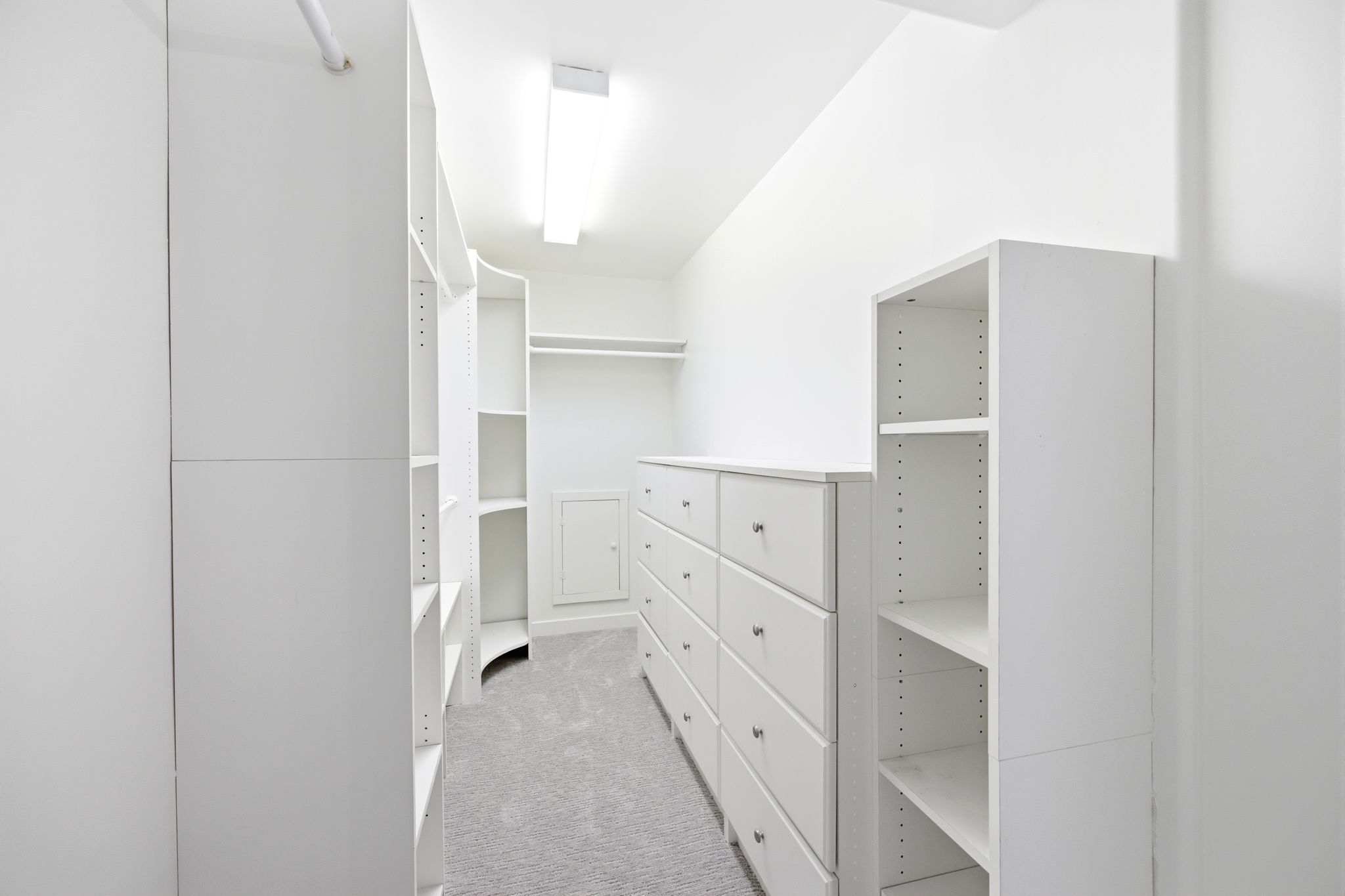 Walk-in closet featuring built-in white cabinetry, integrated shelving, an extensive dresser with silver hardware, and soft gray carpeting