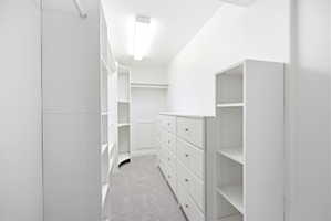 Walk-in closet featuring built-in white cabinetry, integrated shelving, an extensive dresser with silver hardware, and soft gray carpeting