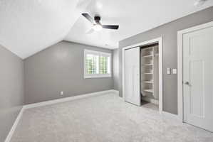 Carpeted room featuring a ceiling fan with integrated lighting, a window with white plantation shutters, and a closet with shelving and a hanging rod