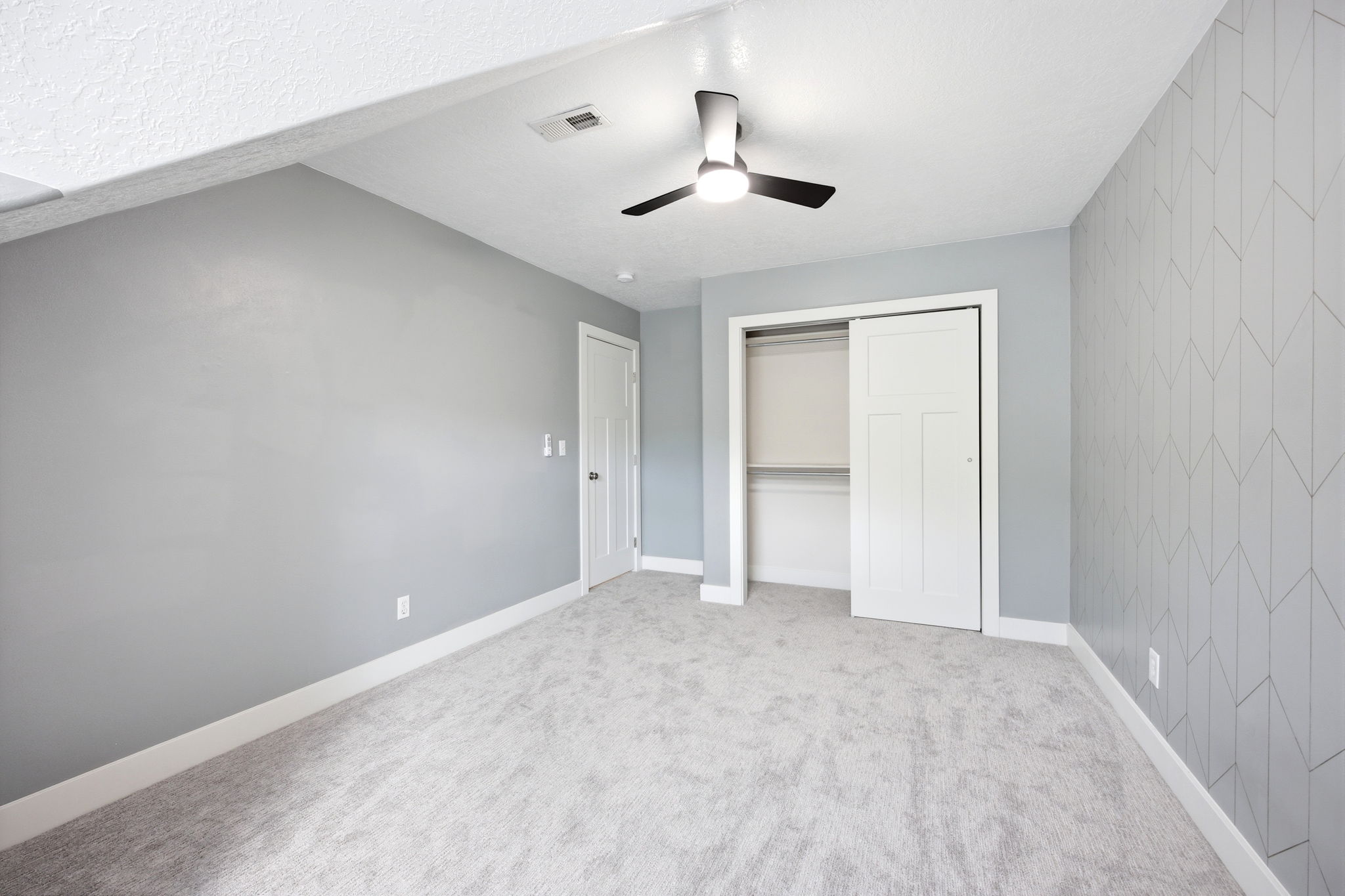 Room featuring light gray walls, gray carpeting, and a decorative accent wall