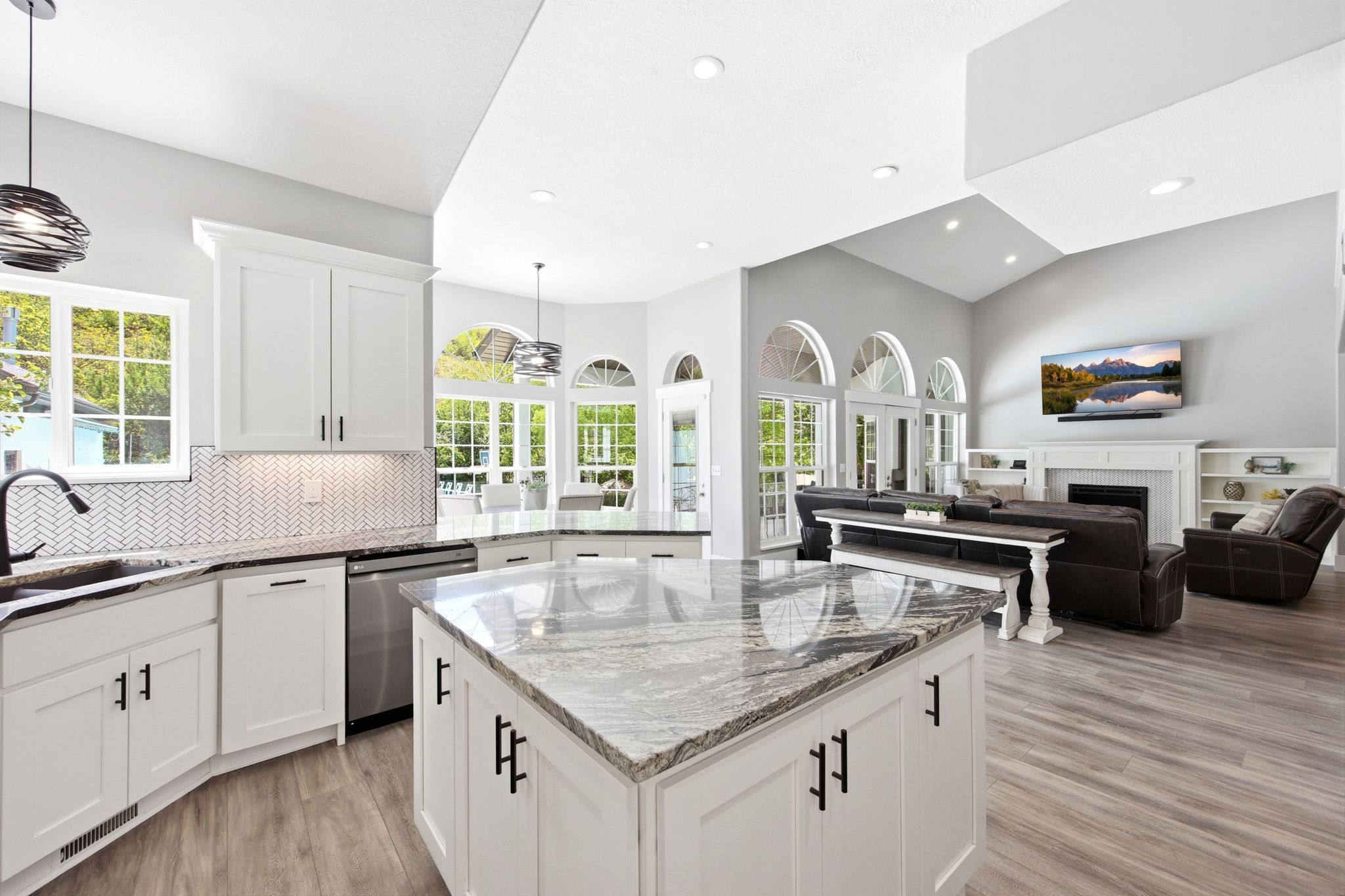 Spacious kitchen featuring an island with a stone countertop, white cabinetry with matte black hardware, stainless steel appliances, a herringbone tile backsplash, and wood-finish flooring