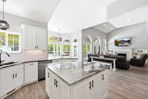 Spacious kitchen featuring an island with a stone countertop, white cabinetry with matte black hardware, stainless steel appliances, a herringbone tile backsplash, and wood-finish flooring