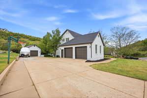 Exterior featuring a white facade, dark roofing, a three-car garage, and a concrete driveway