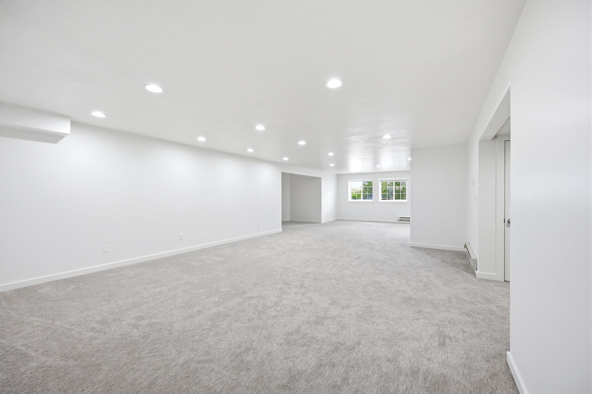 Spacious room featuring light gray carpeting, recessed ceiling lighting, and multiple windows providing natural illumination